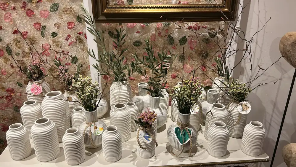 Weiße Keramikvasen mit Olivenzweigen und Trockenblumen auf einem Tisch.